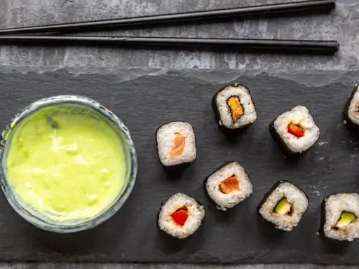 Sushi mit Lachs, Avocado und Paprika, dazu eine grüne Soße. Ist Wasabi gesund? Ja, es ist bekannt für seine entzündungshemmenden Eigenschaften.
