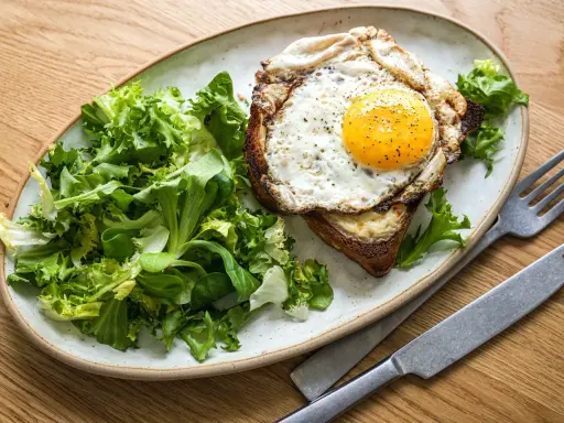 Ein Croque Madame mit Spiegelei, Käse und Toast, serviert mit frischem Salat.