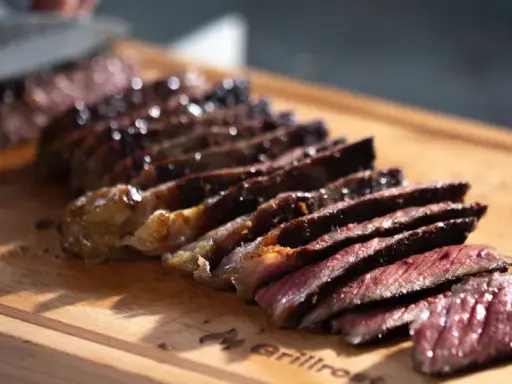 Saftiges Steak, auf einer Plancha zubereitet, wird auf einem Holzbrett in Scheiben geschnitten.