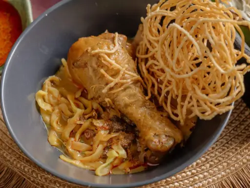 Khao Soi: Hühnerkeule in cremiger Kokosmilch-Currysauce mit weichen und knusprigen Nudeln.