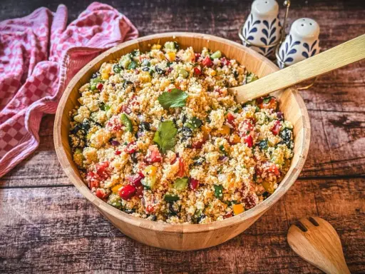 Ein bunter Couscous-Salat mediterran mit Tomaten, Gurken, Paprika und Oliven in einer Holzschüssel, bereit zum Servieren.