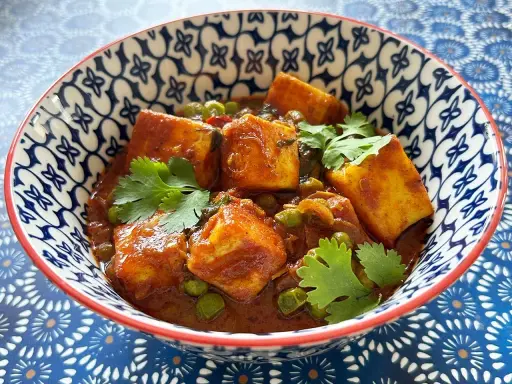 Schüssel mit cremigem Mattar Paneer, garniert mit Koriander. Die Sauce ist reichhaltig und rotbraun, mit Erbsen und würzigen Paneer-Würfeln.