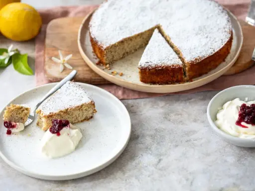 Ein saftiger Ricotta Mandel Kuchen, bestäubt mit Puderzucker, serviert mit einer Kugel Sahne und roter Grütze.
