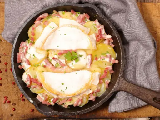 Herzhaftes Tartiflette-Rezept in Gusseisenpfanne: Kartoffeln, Speck und geschmolzener Käse, garniert mit Petersilie.