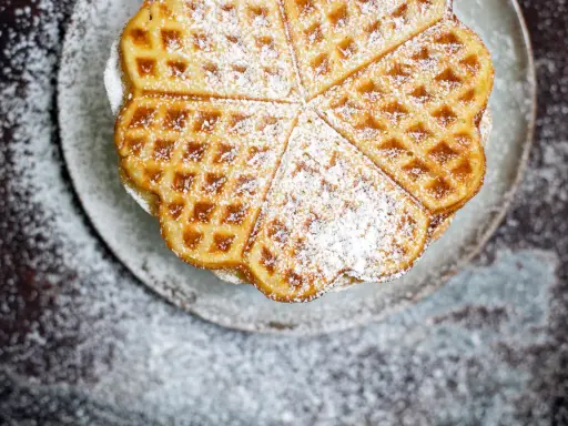 Herzförmige Waffeln mit Puderzucker bestreut, serviert auf einem Teller. Ein Genuss, der an Sommer und Kokosmilch erinnert.