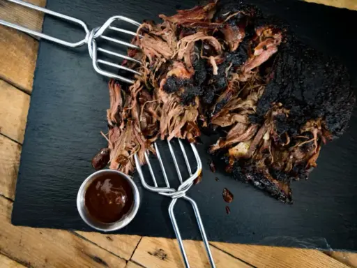 Saftiges pulled beef mit dunkler Kruste, serviert mit BBQ-Sauce.