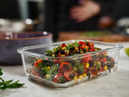 Frischer schwarze bohnen salat mit Mais, Tomaten und Kräutern in einer Glasbox, bereit zum Mitnehmen.