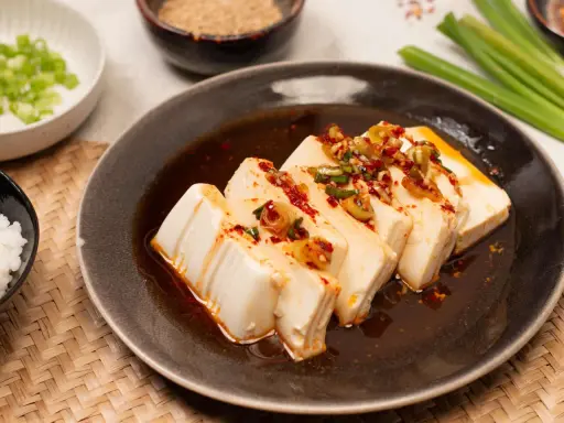 Seidiger Tofu, ein einfaches silken tofu recipe, serviert mit Frühlingszwiebeln und Chili-Öl auf einem dunklen Teller.