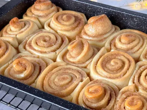 Frisch gebackene, fluffige Zimtschnecken in einer Backform. Sie duften nach Zimt und Zucker und sind bereit zum Genießen.
