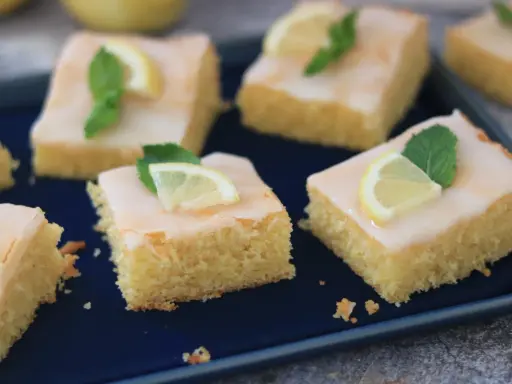 Saftige Kuchenstücke mit Zitronenguss, garniert mit Zitronenspalten und Minze. Ein Genuss, der nach dem besten zitronenkuchen der welt schmeckt.