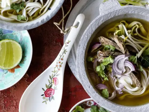 Ein dampfendes Pho-Rezept mit zarten Rindfleischscheiben, Reisnudeln, Sojasprossen und frischem Koriander in einer aromatischen Brühe. Dazu Limettenspalten.