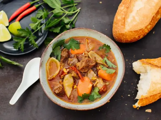 Herzhaftes Bo Kho, ein vietnamesischer Rindfleischeintopf mit Karotten und Kräutern, serviert mit Baguette.