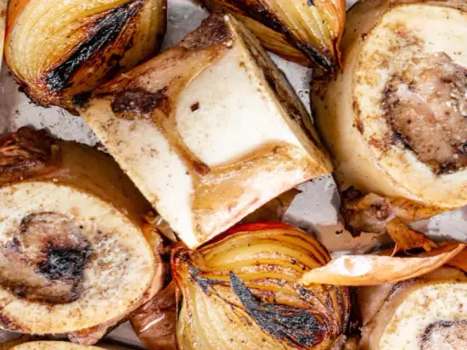 Rinderknochen auskochen Rezept: Geröstete Rinderknochen und Zwiebeln auf einem Blech, bereit für eine herzhafte Brühe.