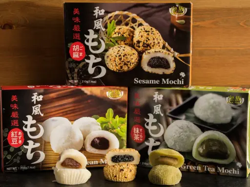 Verschiedene Sorten japanischer Reiskuchen (Mochi) mit Sesam, roter Bohne und grünem Tee, auf dunklem Untergrund vor Holz.