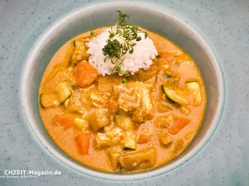 Ein cremiger Lachs Curry mit Reis und Gemüse, garniert mit frischen Sprossen.