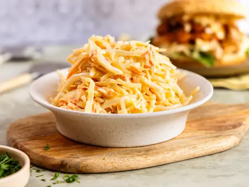 Schüssel mit cremigem Coleslaw, perfekt für das **rezept coleslaw original**. Im Hintergrund ein Burger.