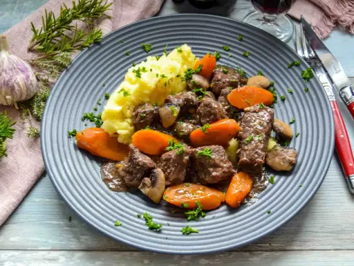 Herzhaftes Boeuf Bourguignon Rezept mit zartem Rindfleisch, Karotten, Pilzen und Kartoffelpüree, garniert mit Petersilie.