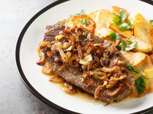 Ein saftiges Stück Rindfleisch, bedeckt mit goldbraunen Röstzwiebeln, serviert mit knusprigen Bratkartoffeln. Das ist der beste Zwiebelrostbraten!