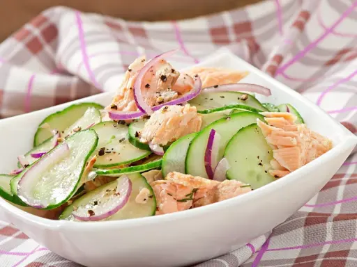 Frischer Gurkensalat mit zarten Lachsstücken und roten Zwiebelringen, gewürzt mit Pfeffer. Ein leichter und gesunder Salat.