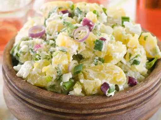 Herzhafter Kartoffelsalat mit Meerrettich, verfeinert mit Frühlingszwiebeln und roten Zwiebelringen, serviert in einer Holzschale.