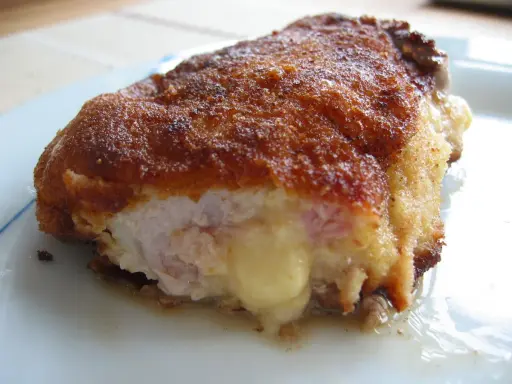 Ein goldbraunes Cordon Bleu, das innen mit geschmolzenem Käse und Schinken gefüllt ist. Seine Herkunft ist oft umstritten, aber der Geschmack ist unbestritten.