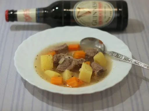 Herzhafter Irish Stew mit Kartoffeln und Karotten in einer Schüssel, daneben eine Flasche Guinness.