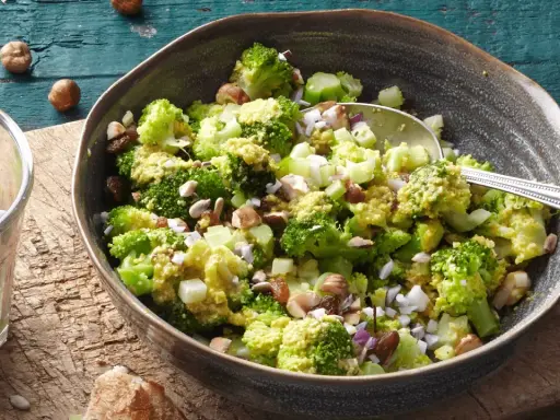Ein einfacher Brokkoli-Salat mit Nüssen und Rosinen, serviert in einer Schüssel auf einem Holztisch.