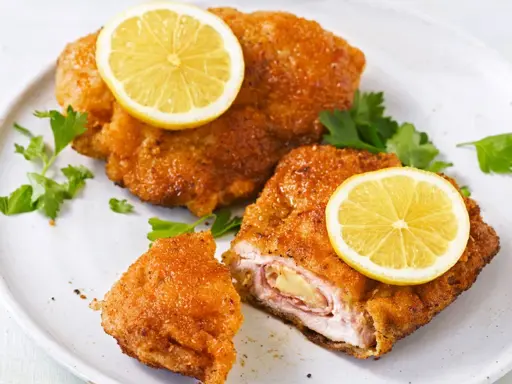 Zwei goldbraune Cordon Bleu mit geschmolzenem Käse und Schinken, garniert mit Zitronenscheiben und Petersilie.