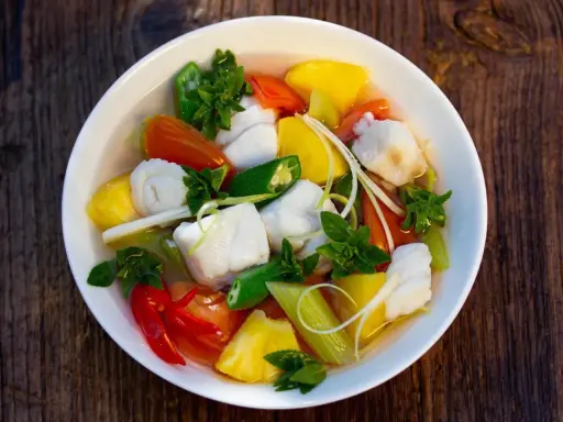 Ein Schüssel mit Canh Chua, einem vietnamesischen Fisch-Gemüse-Eintopf, mit Ananas, Tomaten, Okra und Kräutern.