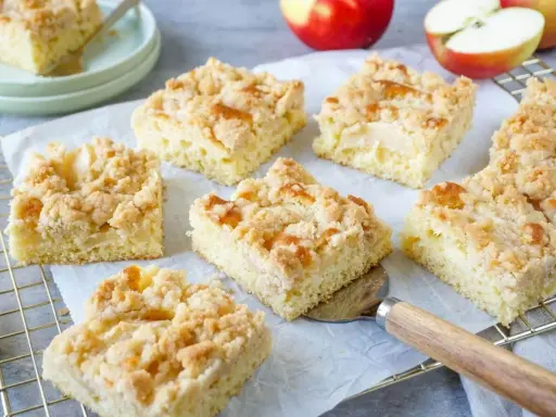 Saftige Stücke vom besten Apfelkuchen mit Streusel, frisch gebacken und bereit zum Genießen. Äpfel liegen daneben.