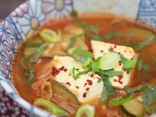 Heißes, würziges Sundubu Jjigae mit weichem Tofu, Kimchi und Frühlingszwiebeln in einer bunten Schüssel.