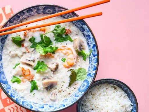 Khao tom, eine cremige Reissuppe mit Garnelen, Pilzen und Koriander, wird mit einem Schälchen Reis serviert.