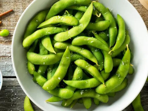 Salzige Edamame-Schoten in einer Schüssel, bereit zum Genießen. So isst man Edamame: die Schote aufbeißen und die Bohnen herausdrücken.