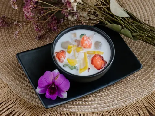 Schüssel mit cremigen asiatischen Nachspeisen, garniert mit Früchten und einer Orchidee.