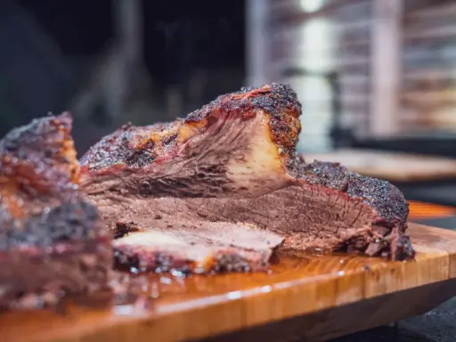 Saftiges Rind Brisket mit dunkler Kruste, auf einem Holzbrett serviert. Der Rauch steigt auf und verspricht ein zartes Geschmackserlebnis.