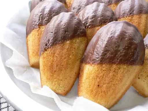 Eine Reihe von Madeleines, die zur Hälfte in Schokolade getaucht sind, warten darauf, gegessen zu werden.
