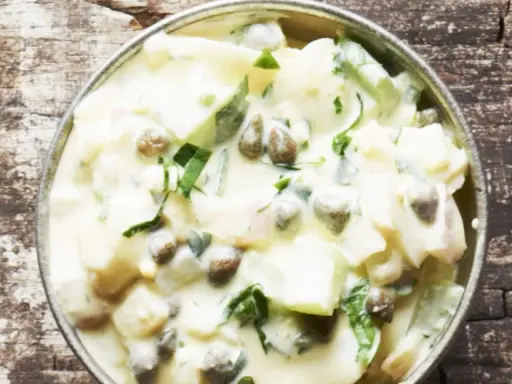 Cremiger Kartoffelsalat mit Kapern und frischen Kräutern, serviert in einer Metallschale auf rustikalem Holz.