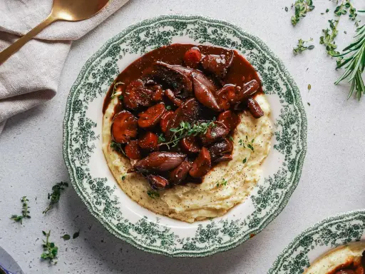 Herzhaftes Pilz-Bourguignon auf cremigem Kartoffelpüree, garniert mit frischen Kräutern. Ein Genuss für jeden Gaumen.