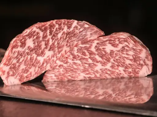 Zwei saftige Steaks vom Kobe Rind liegen auf einem metallischen Untergrund. Ihr auffälliges Marmormuster aus Fett und Fleisch verspricht ein einzigartiges Geschmackserlebnis.