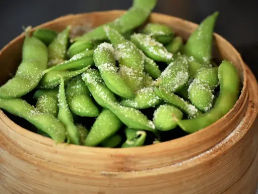 Frische Edamame-Schoten, leicht gesalzen, bereit zum rohen Essen. Ein gesunder Snack in einem Bambuskorb.