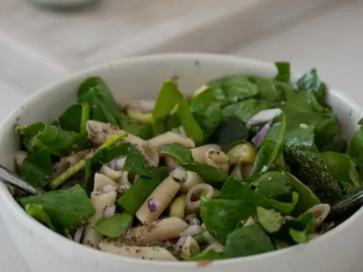 Ein frischer nudelsalat mit spargel, garniert mit Spinat und roten Zwiebeln, bereit zum Genießen.
