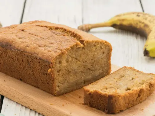 Saftiges Bananenbrot mit Skyr, frisch gebacken und auf einem Holzbrett angerichtet. Eine Banane liegt daneben.