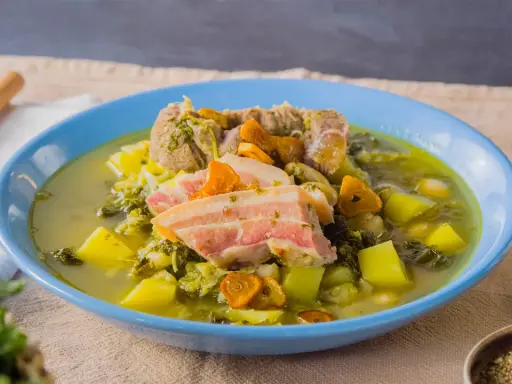 Herzhafter spanischer Eintopf mit Fleisch, Kartoffeln, Grünkohl und Karotten in einer blauen Schüssel.