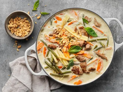 Herzhaftes Thai Curry mit Rindfleisch, zarten Möhren, grünen Bohnen und Maiskolben in cremiger Kokosmilch, garniert mit Erdnüssen und Basilikum.