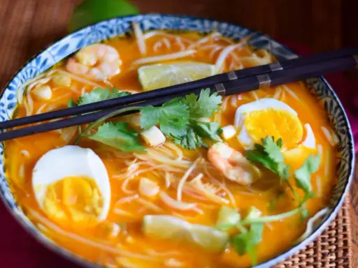Eine Schüssel mit köstlicher Laksa Suppe, garniert mit Garnelen, Ei, Limette und Koriander.
