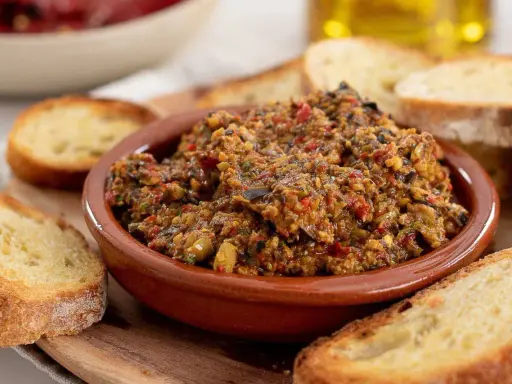 Herzhafte Tapenade deutsch in einer Tonschale, umgeben von geröstetem Brot. Ein Genuss für jeden Feinschmecker.