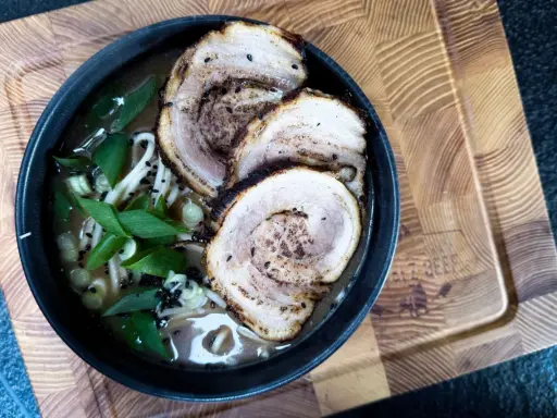Schüssel mit Ramen-Nudeln, Brühe, Frühlingszwiebeln und drei Scheiben Chashu-Schweinebauch. Ein köstliches Chashu-Rezept!