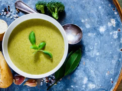 Grüne Detox-Suppe mit frischem Basilikum, dazu Baguettescheiben, Knoblauch und Brokkoli.