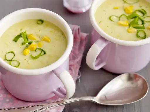Zwei Tassen cremiger Maissuppe mit Kokosmilch, garniert mit Maiskörnern und Frühlingszwiebeln.