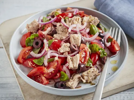 Frischer Tomaten-Thunfisch-Salat mit roten Zwiebeln und Oliven, garniert mit Basilikum. Ein leichter und gesunder Genuss.